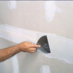 painter applying drywall compound to wall before painting